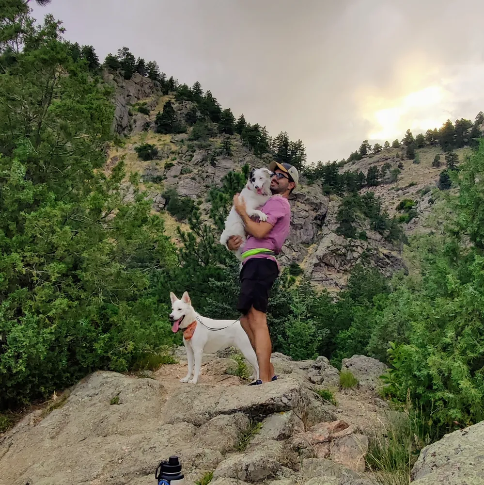 Grant on a rock at sunset holding Drey, with Luna beside him