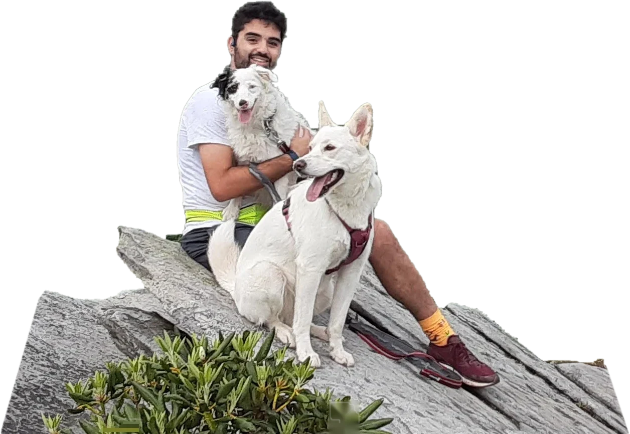 Grant smiling on a mountain ledge, holding Drey, with another of his dogs in front