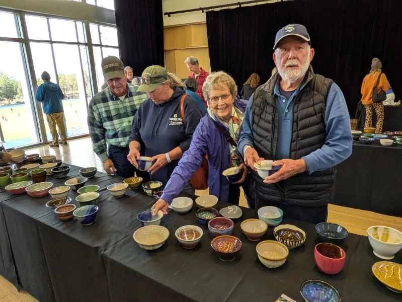 Guests holding handmade ceramic bowls at a long table of bowls