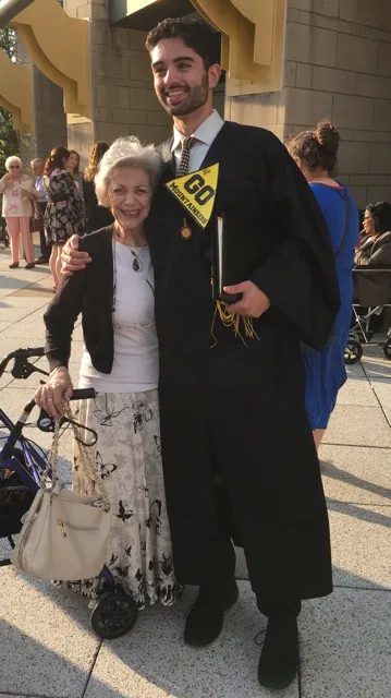 Grant in his graduation gown with an App State pennant, smiling with his arm around a loved one