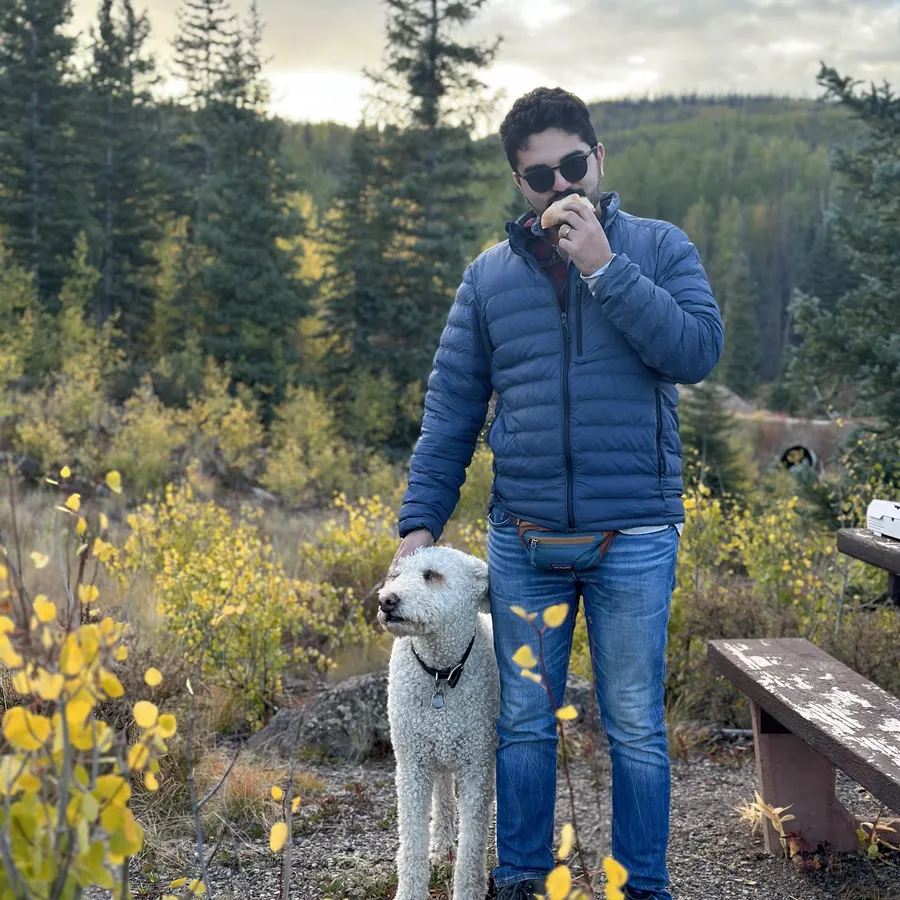 Grant in sunglasses and a blue puffer jacket on a fall trail with Luna
