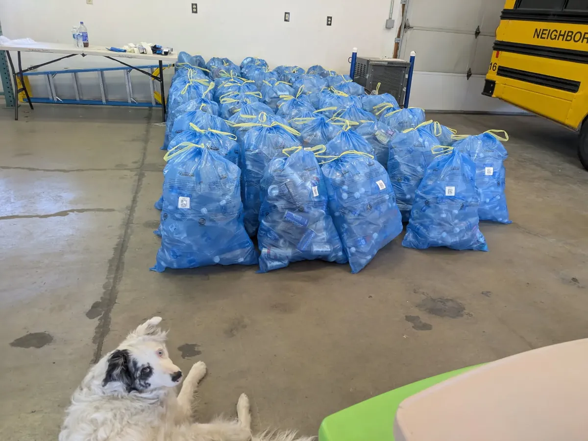 Rows of tied blue bags full of cans and bottles in a garage, with Drey lying in the foreground