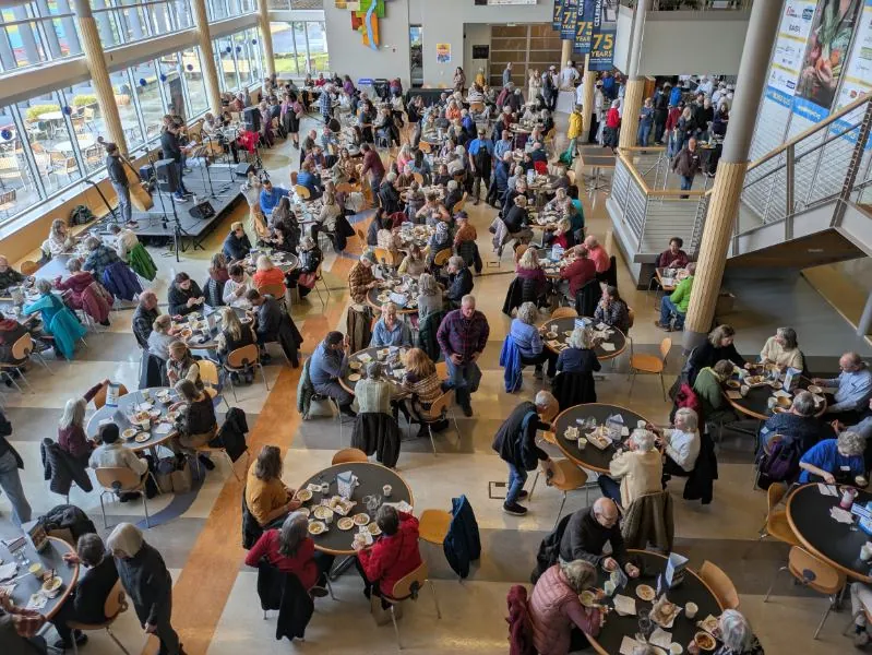 A packed atrium of round tables seen from above, with live music on a small stage